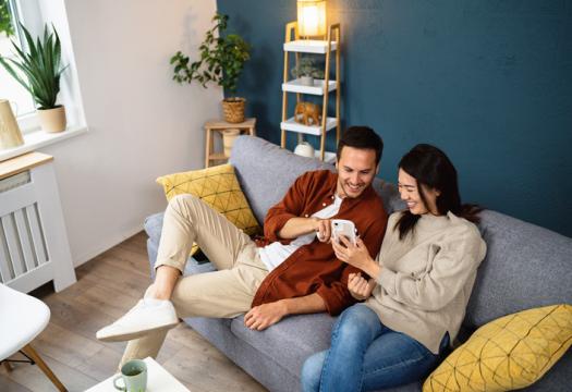 Young couple using smartphone device while relaxing on a sofa at home | Merry Maids