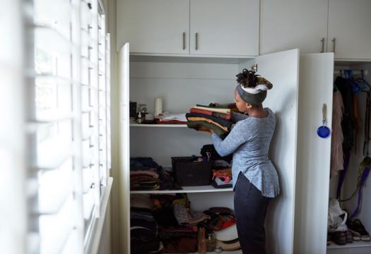 Woman putting folded clothes away in the closet to organize her space. | Merry Maids®