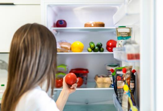 Young pretty woman taking fresh healthy tomato vegetables from refrigerator | Merry Maids