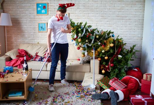 Young man wearing and surrounded by Christmas themed decorations cleaning up after the new year. | Merry Maids®